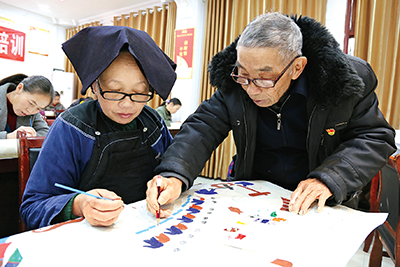 图为近日,该县乡土人才赵元桥(右)在指导群众制作农民画.罗文刚 摄